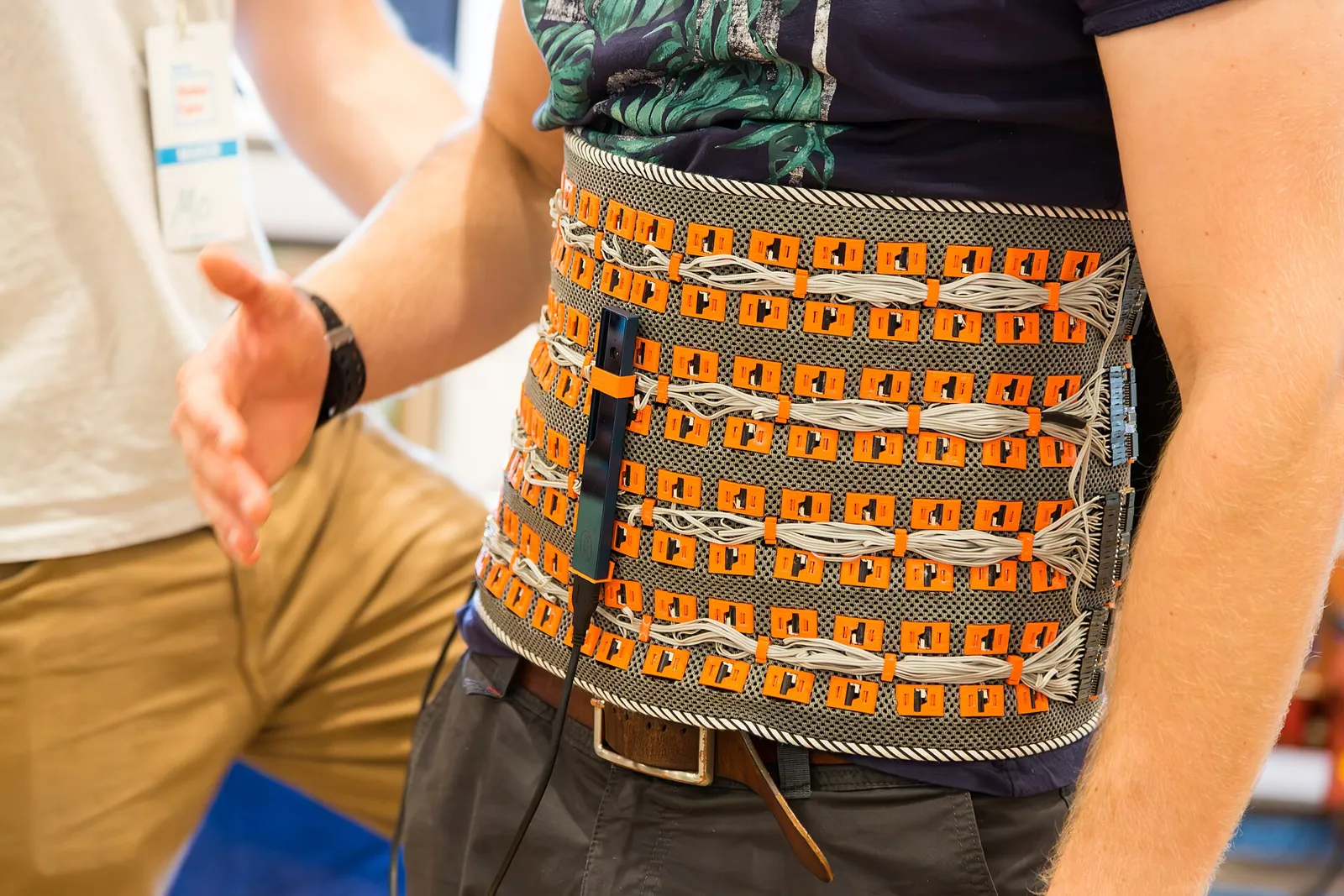 Ein Mann trägt einen breiten, orangefarbenen Gürtel voller LEDs und Kabel.