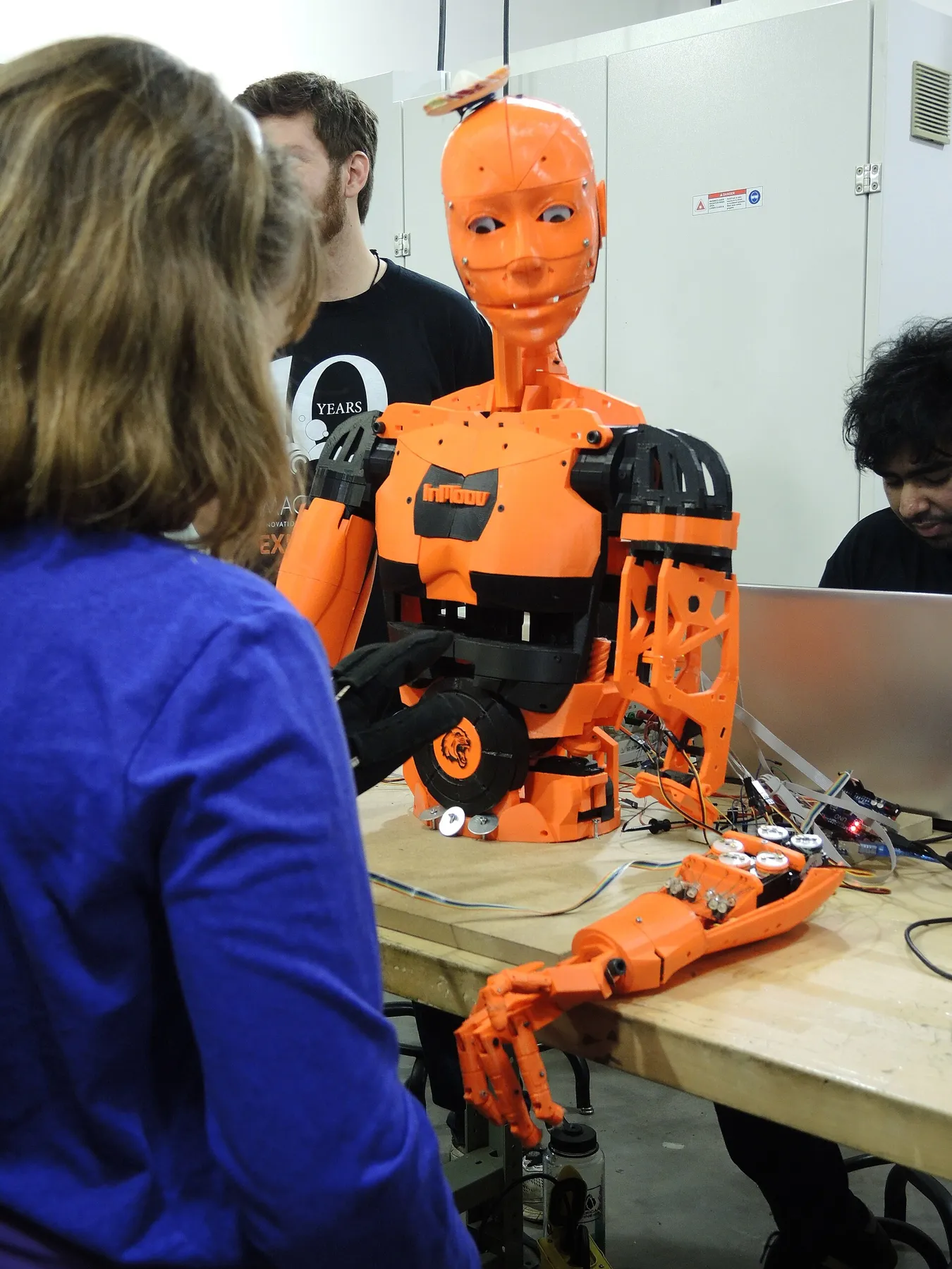 Ein Mädchen arbeitet an InMoov, einem orangefarbenen Roboter aus dem 3D-Drucker.